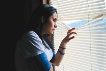 Young woman peeking through venetian blinds Young woman peeking through venetian blinds