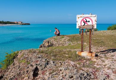 Man looking at the ocean next to a No Swimming sign Man looking at the ocean next to a No Swimming sign