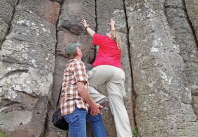A man giving a women a leg up to climb a cliff