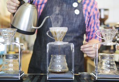 A barista's hands are seen pouring boiling water to make filter coffee.