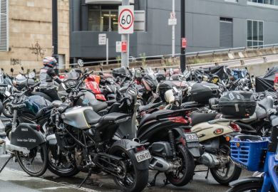 A dense parking area filled with various motorcycles and scooters, with street signs in the background.