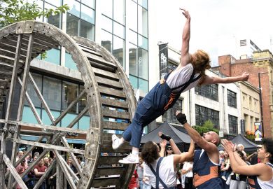 A performer on a rolling wooden wheel falls backwards, knowing that her team members will catch her  A performer on a rolling wooden wheel falls backwards, knowing that her team members will catch her