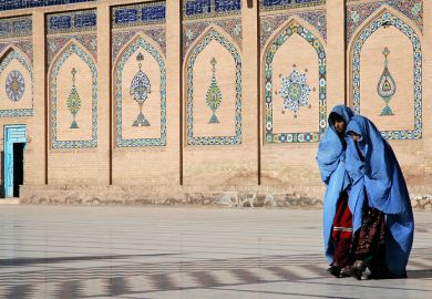 Two women in blue burqas walk at the front of a mosque with a door open, symbolising an open university