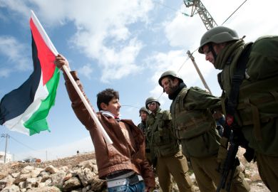 Al-Masara, Occupied Palestinian Territories - January 27, 2012 A Palestinian youth waves a flag while confronting Israeli soldiers in a protest against the Israeli separation barrier in the West Bank down of Al-Masara.