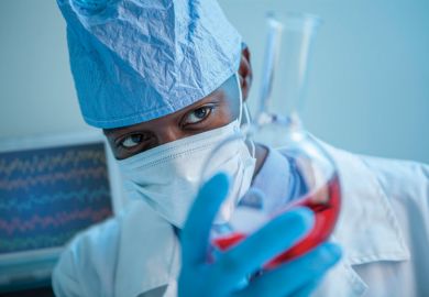 An academic studying red liquid in a glass flask An academic studying red liquid in a glass flask