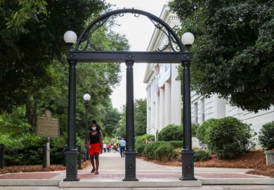 Athens, Georgia - August 27, 2021 A student wearing a protective face mask walks through the Arch at the entrance to the University of Georgia's historic North Campus.