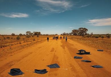 People walk down a dusty outback road, their abandoned mortar boards behind them People walk down a dusty outback road, their abandoned mortar boards behind them