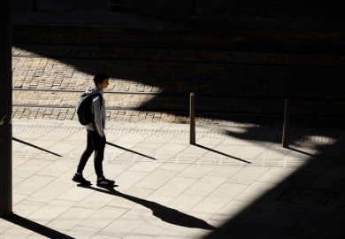 Belgrade, Serbia - October 26, 2020 One teenage boy standing alone waiting for a tram on bus stop in sunlight, high angle view from behind, with shadows