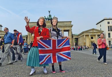Pair wearing queen masks and holding Union Jack in front of Brandenburg Gate Pair wearing queen masks and holding Union Jack in front of Brandenburg Gate