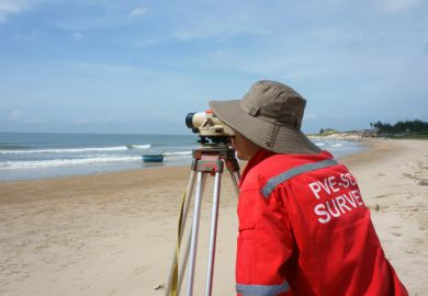 Binh Thuan, Viet Nam - October 21, 2014 Asian engineer work on Vietnamese beach, man looking in theodolite to survey sea level, measurement device set on tripod, Vietnam, Oct 21, 2013