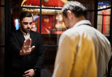 A security guard blocks a doorway, symbolising university access