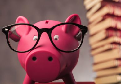 A piggy bank beneath a pile of books A piggy bank beneath a pile of books, symbolising open access costs