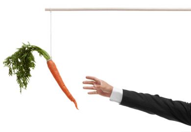Businessperson's hand reaching for carrot on stick Businessperson's hand reaching for carrot on stick
