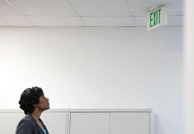 Businesswoman looking up at office 'Exit' sign
