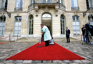 A woman vacuums a red carpet outside a posh building