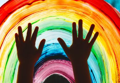Close-up photo of child's hands touch painting rainbow on window