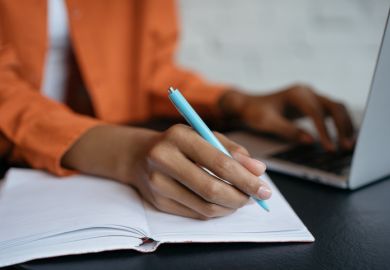 Close-up shot of student hand holding pen and writing in notebook