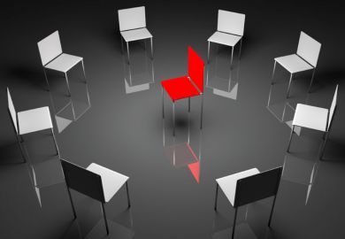 A circle of grey chairs with one red chair in the centre