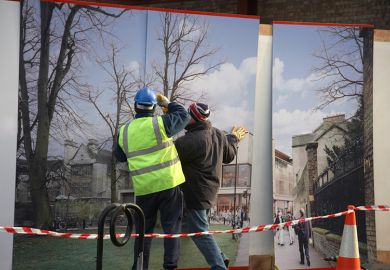 Construction workers installing hoarding around a property development site, to illustrate that universities must choose between physical or digital development.