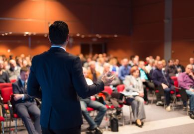 A suited man speaks at a meeting, symbolising corporatisation
