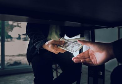 A man passes hundred-dollar bills under the table, illustrating corruption
