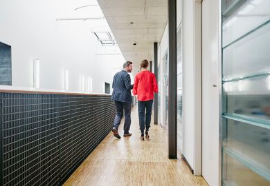 Older man and woman in university corridor, illustrating staff-student relationships.