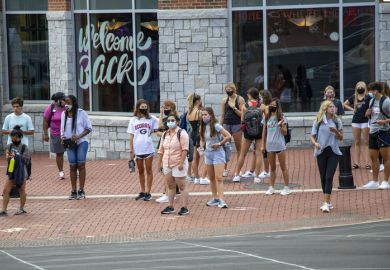 Athens, Georgia - August 20, 2020 During the COVID-19 pandemic on the first day of the Fall semester, students in protective face masks gather at a crossing light in front Bolton Dining Commons at the University of Georgia.