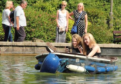 Female students using smartphones on boating lake