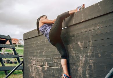 Female participant in an obstacle course climbing a wall Female participant in an obstacle course climbing a wall illustrating gender inequality in economics