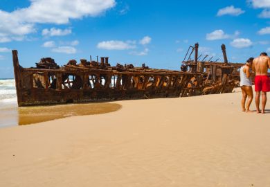 Fraser Island Australia; Two tourists on beach by Maheno shipwreck rusting away on beach