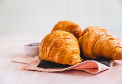 Fresh crispy croissants with red berry jam on slate board, pink background