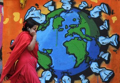 A woman on a phone walks past a graffiti depicting world map affected with Coronavirus. India. A woman on a phone walks past a graffiti depicting world map affected with Coronavirus. India.