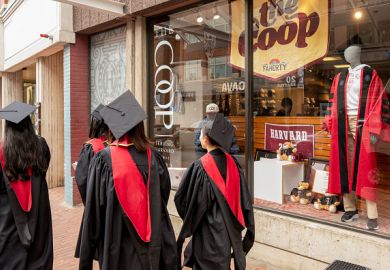Harvard University students wearing graduation gowns walk past a bookstore near the Harvard University campus in Cambridge, Massachusetts, US