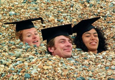 Graduates buried in shingle on Brighton beach, England Graduates buried in shingle on Brighton beach, England