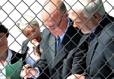 Group of academics in conversation behind chainlink fence Group of academics in conversation behind chainlink fence