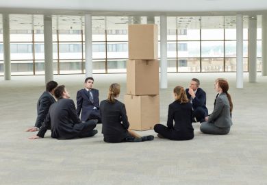 Group of businesspeople sat around pile of cardboard boxes Group of businesspeople sat around pile of cardboard boxes