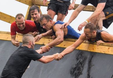 Group of men assisting teammate on obstacle course