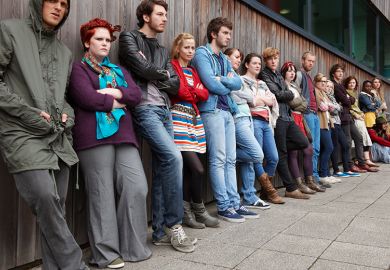 Crowd of grumpy looking students leaning against a wall, to illustrate a rise in student complaints.