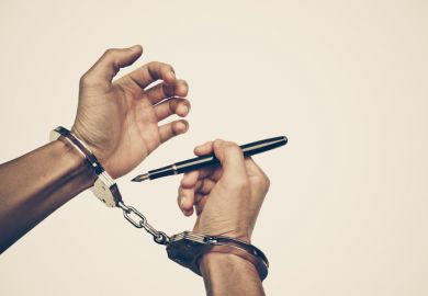 Hands handcuffed,one holding a pen, illustrating the restrictions on research caused by the GDPR