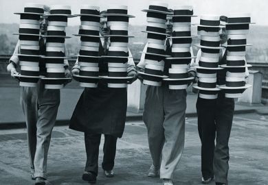 Four people carrying piles of hats