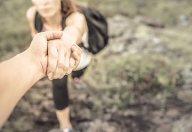 Hikers helping each other climb up mountain