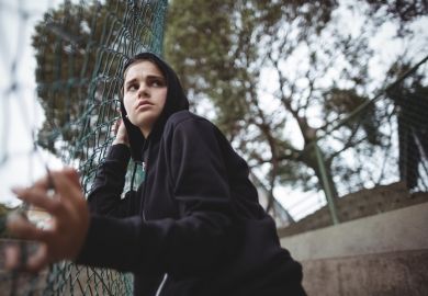 Teenager in a hoody Anxious teenage girl leaning on wire mesh fence