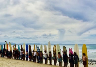 horizontal seascape of surfers with surfboards on sand at surf competition on overcast day at famous place Wategos Beach Byron Bay Australia