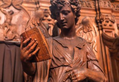 Reading angel holding an old book, wooden statue in 17th century catholic church Saint Charles Borromeo on March 31, 2018.
