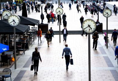 Business people walking in Canary Wharf by the iconic clock installation on Reuters plaza, London's financial district.