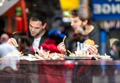 Two men guy friends sitting in fast food cafe looking outside window counter