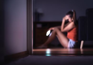 A student reacts with sadness to her mobile phone - online safeguarding should be higher up university agendas