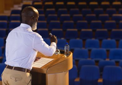 A man at a lecturn with a mic in front of an empty auditorium