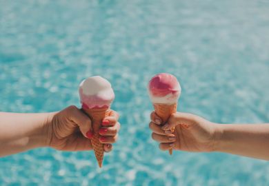 Two hands hold two ice creams by a pool