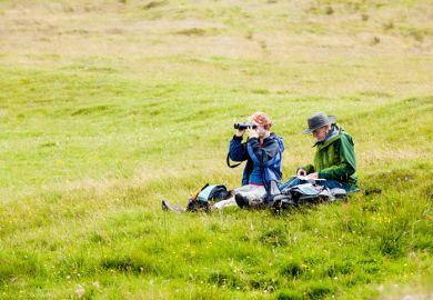 Two senior adults, a man and a woman, sit on the ground in a green meadow in Skye, Scotland Two senior adults, a man and a woman, sit on the ground in a green meadow in Skye, Scotland